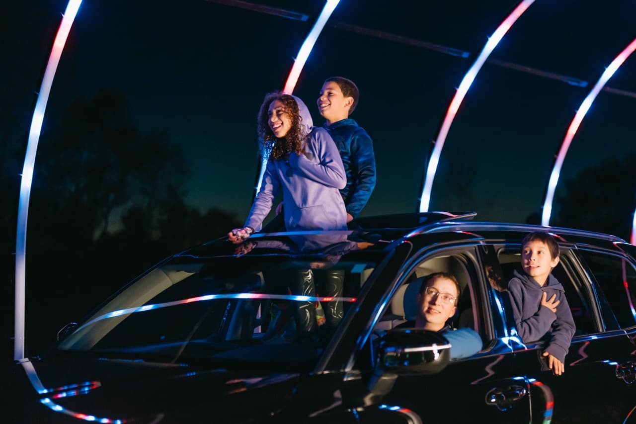 Family enjoying light display from their car with LED arcs in background